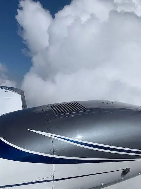 Close-up of the grey and white aircraft fuselage and engine cowling with blue stripes against a cloudy blue sky.