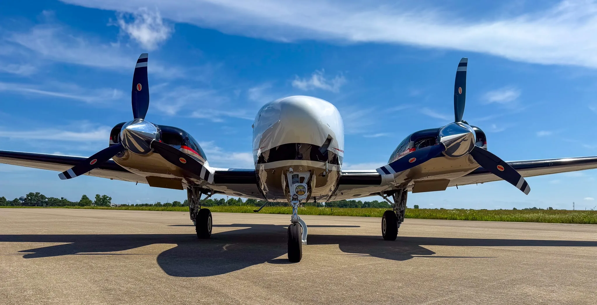 Close-up front view of a white and gold twin-engine Beechcraft Baron G58 on an airfield.