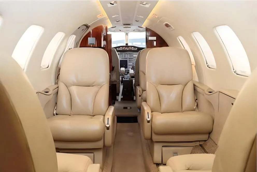View of a luxurious aircraft cabin with beige leather seats and a narrow aisle leading to the cockpit.