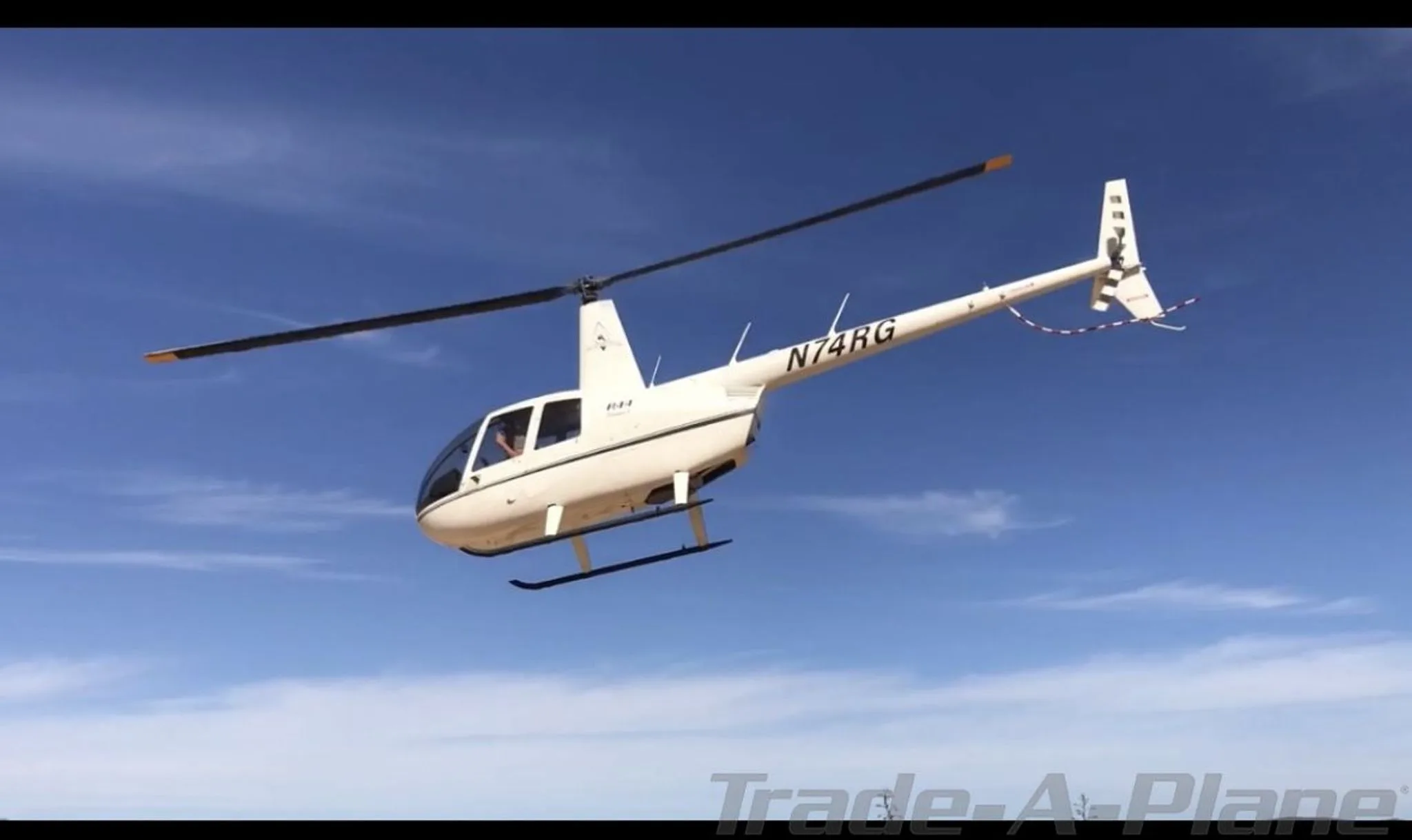 A Robinson R44 Raven I in flight against a clear blue sky.