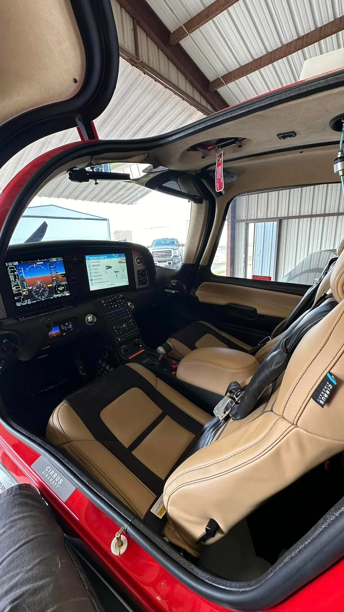 The tan and black leather interior of a Cirrus SR22 aircraft, showing the front seats and the instrument panel through the open door.