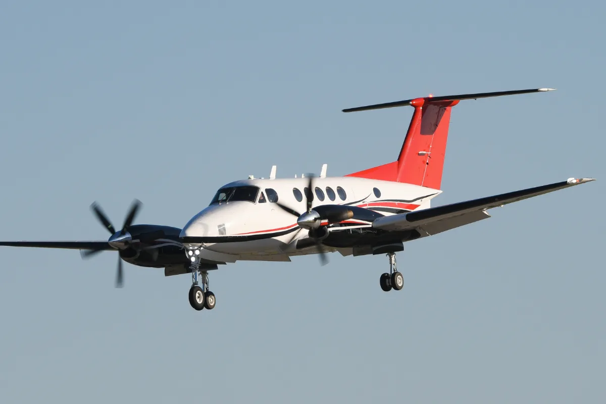A white and red twin-engine turboprop aircraft with landing gear extended, flying against a clear blue sky.