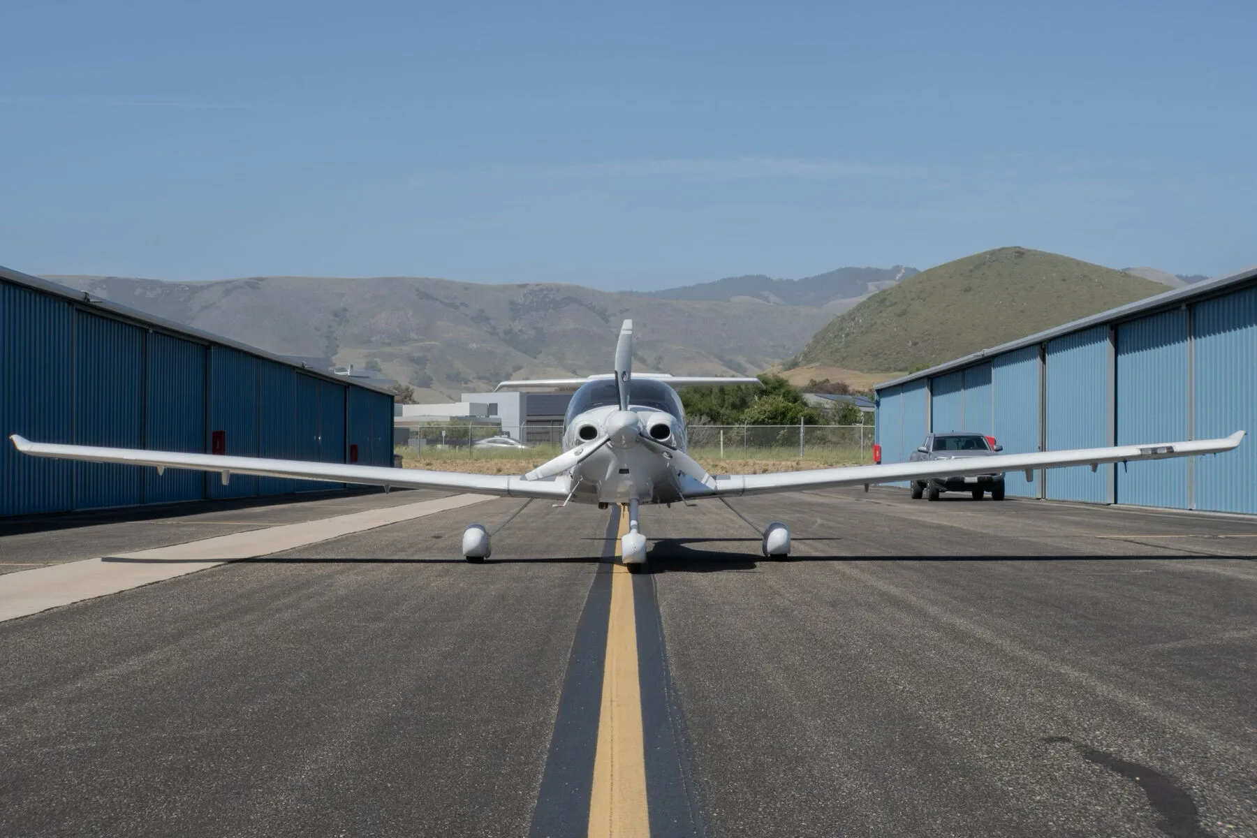 A white Diamond DA40 Star XL aircraft, registration N448US, viewed from the front on an airport runway with hangars and hills in the background.