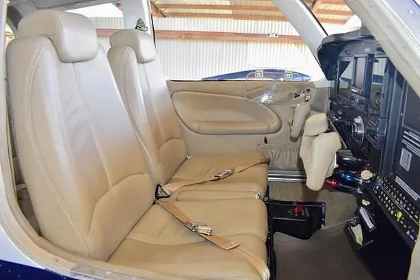 The aircraft's interior cabin showing two light-colored leather seats and a partial view of the cockpit.