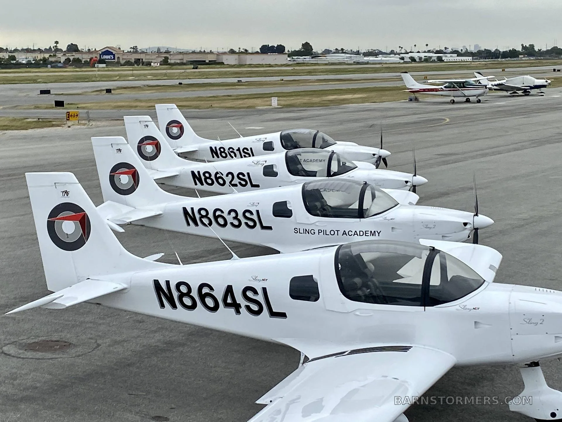A line of white Sling Pilot Academy aircraft (N861SL, N862SL, N863SL, N864SL) parked on an airport tarmac.