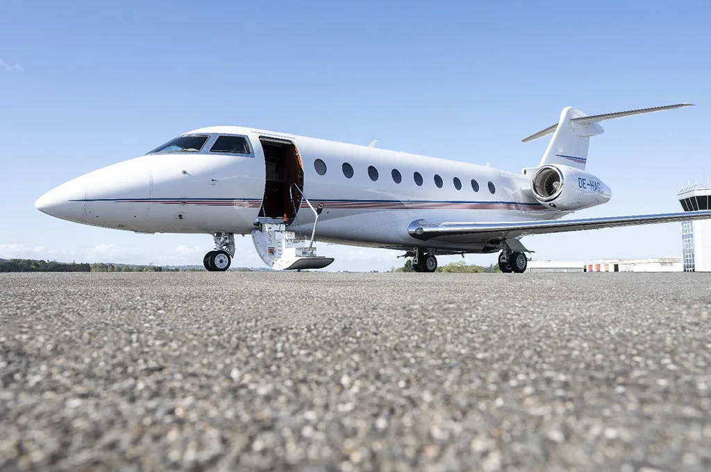 A white business jet with its main door open and stairs extended, parked on an asphalt tarmac.
