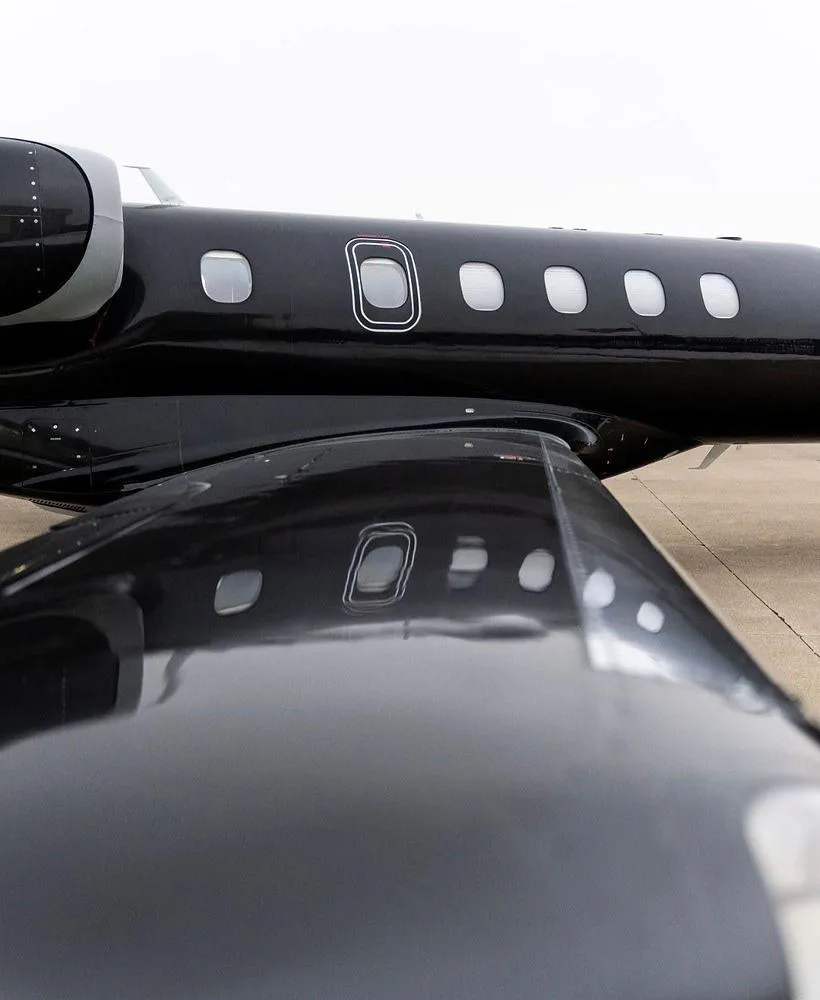 A close-up view of the mid-fuselage and wing of a black Embraer Phenom 300 jet, showing passenger windows.