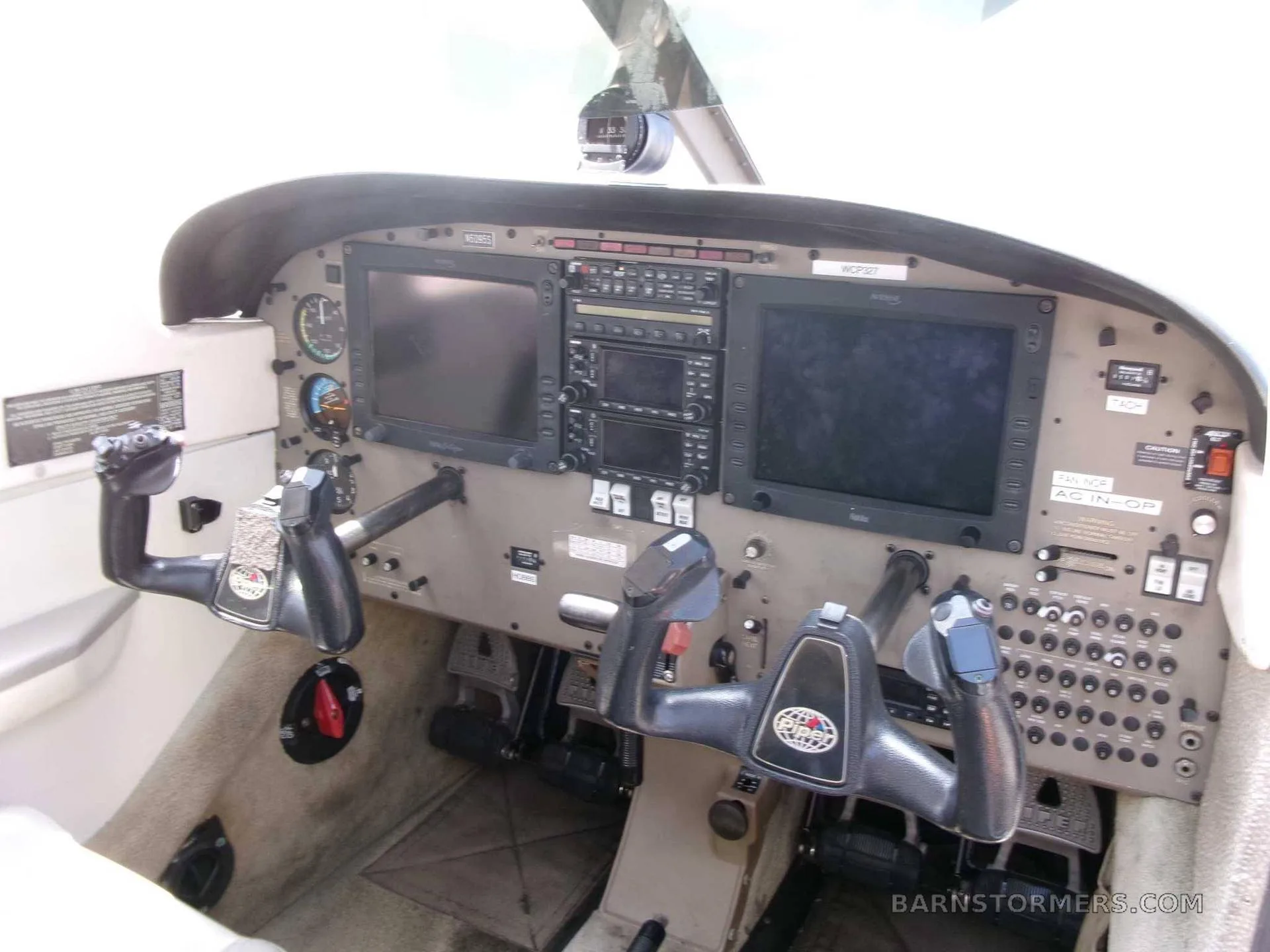 The cockpit of a small aircraft, showing the instrument panel with two large display screens and dual control yokes.