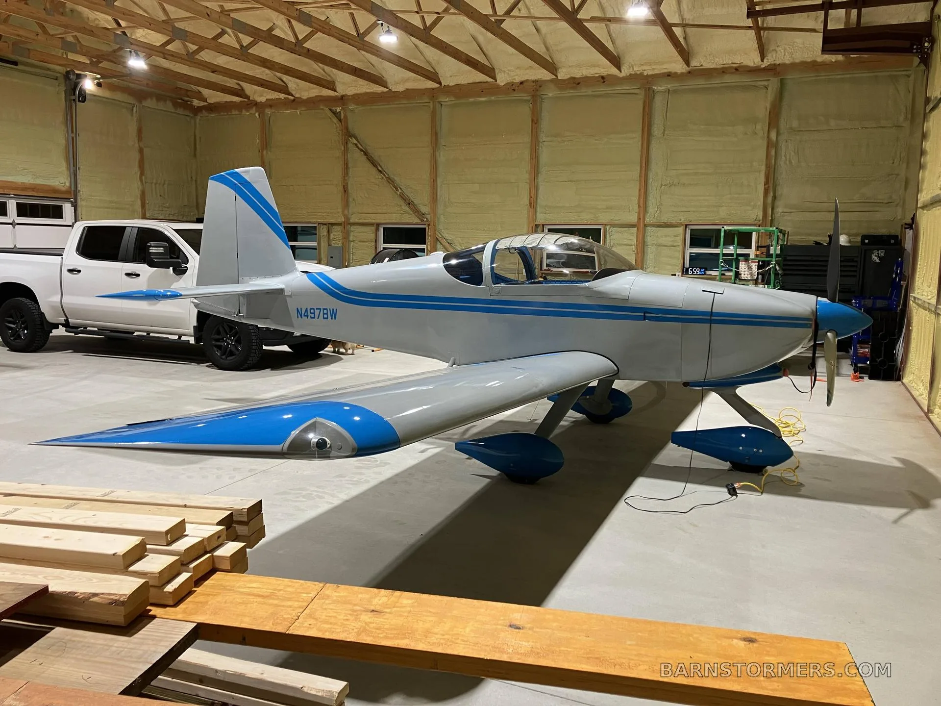 A light gray and blue experimental aircraft, N497BW, parked in a hangar next to a white pickup truck.