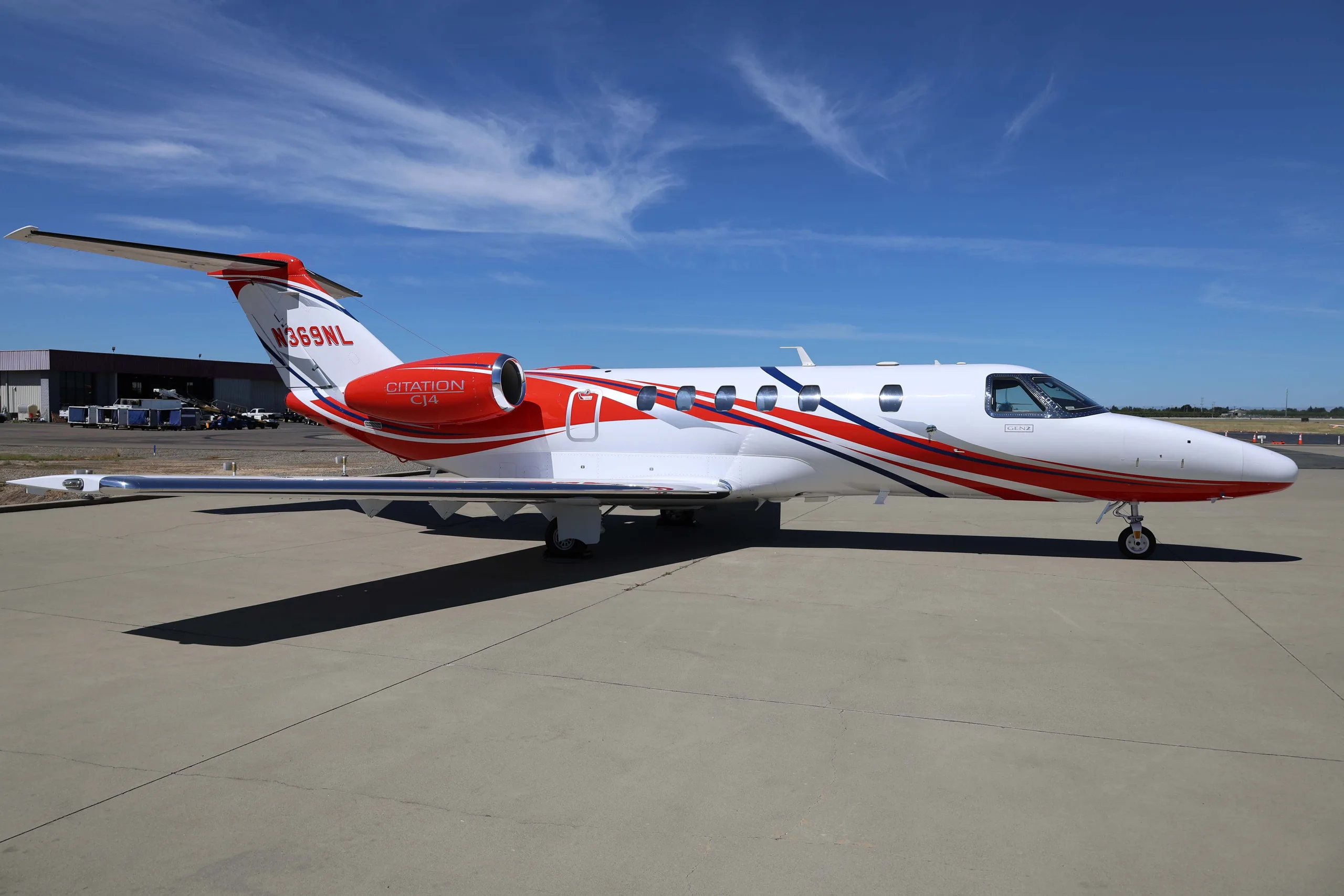 A three-quarter view of the white Cessna Citation CJ4 (N369NL) with red and blue stripes, parked on an airfield.