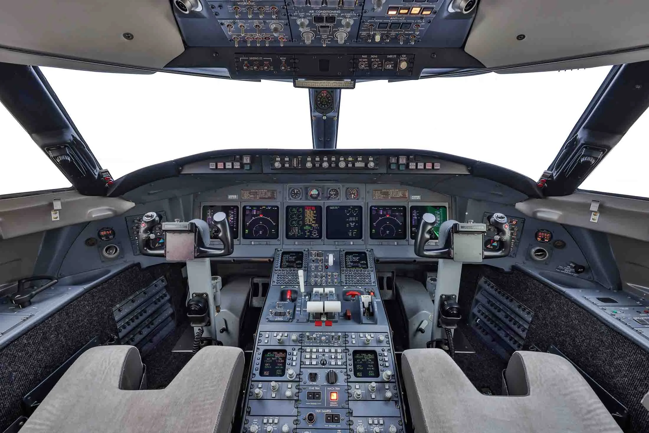 The spacious cockpit of a business jet, featuring multiple digital displays, control yokes, and a central throttle quadrant.