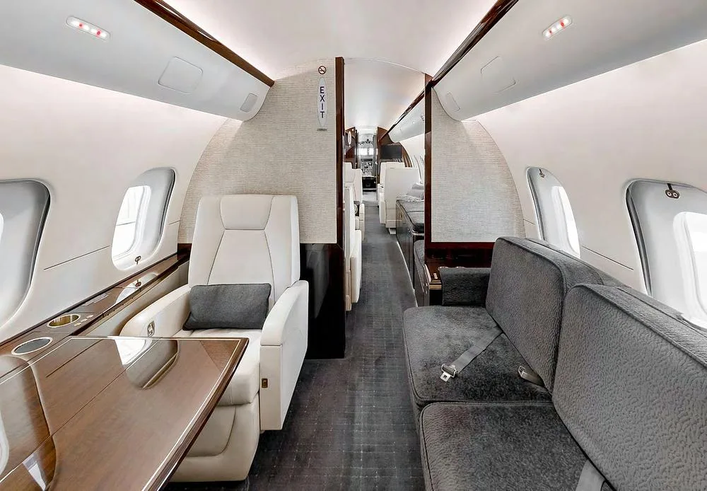A long view of the private jet's elegant cabin interior with grey seating and cream armchairs.