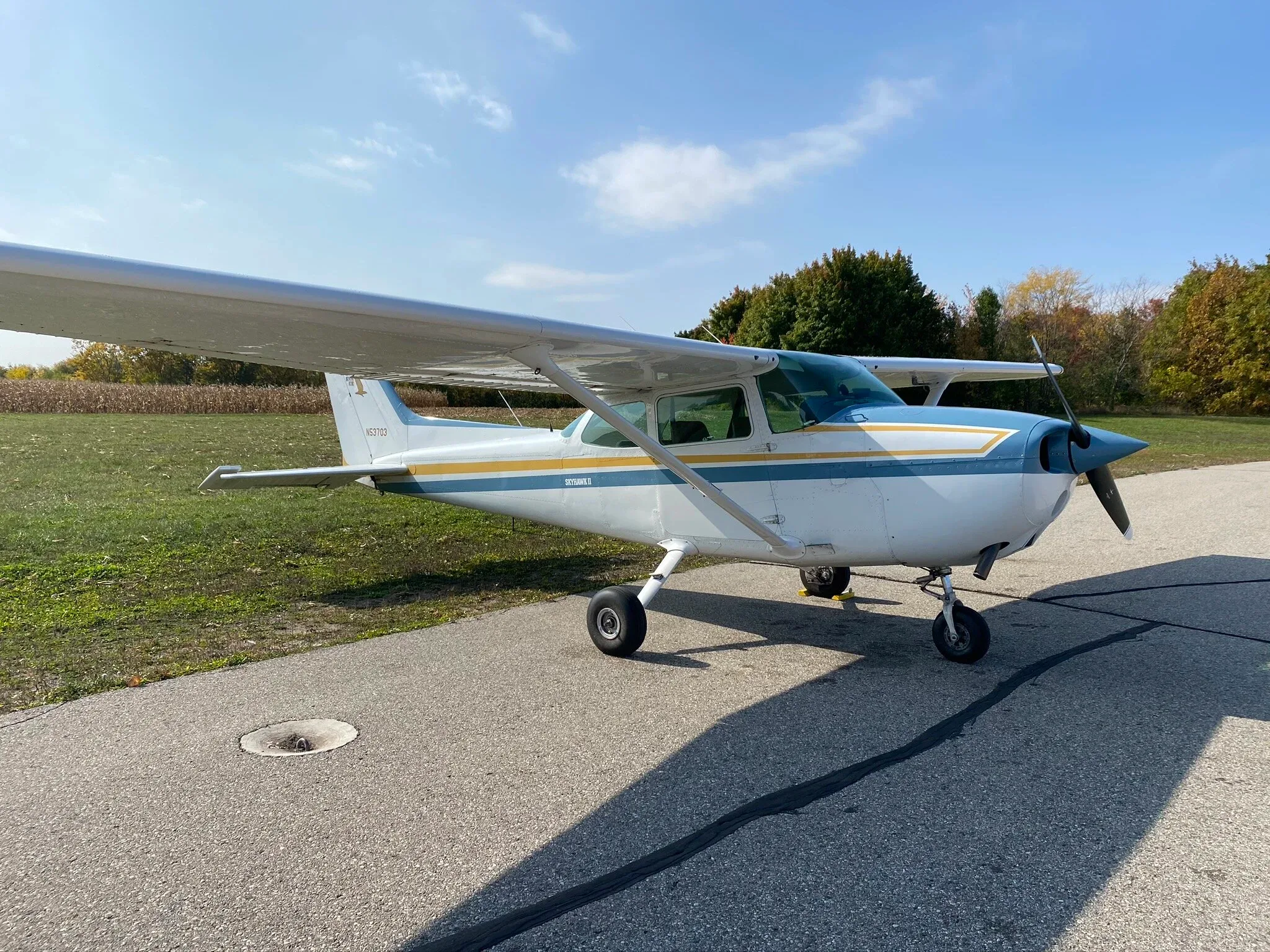 A white and blue Cessna Skyhawk II with yellow stripes parked on an asphalt ramp.