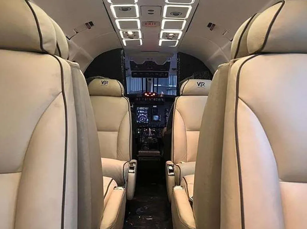 A view from the rear of the cabin looking forward into the cockpit of a private aircraft, showing beige seats.