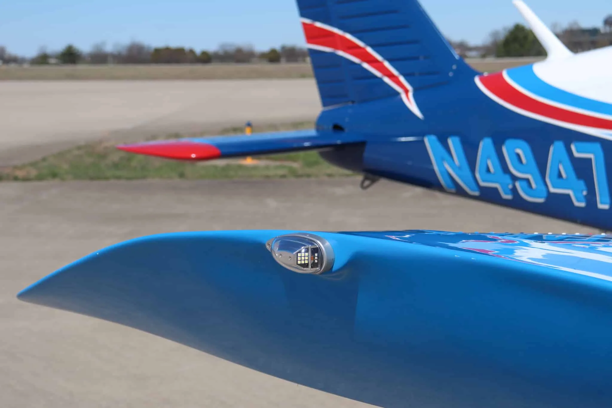 A close-up of the wingtip light and the tail of the blue and white Piper Cherokee aircraft showing the N-number.