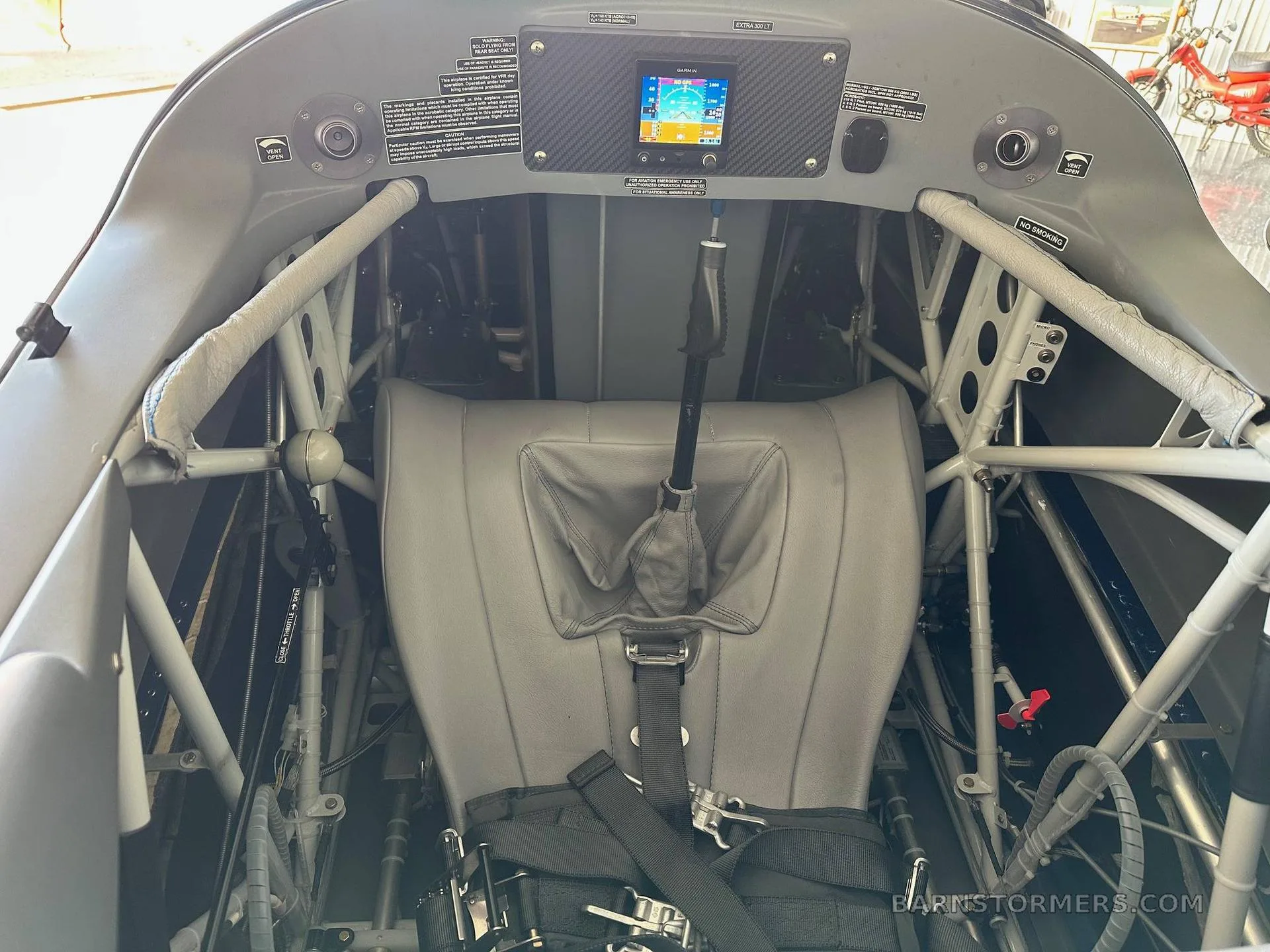 The gray leather single-seat interior of an Extra 300LT aircraft, showing the roll cage and control stick.