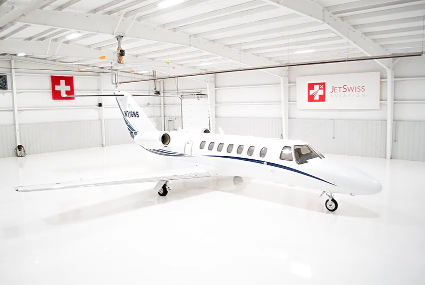 A white business jet with blue stripes (N716NS) parked in a brightly lit hangar.
