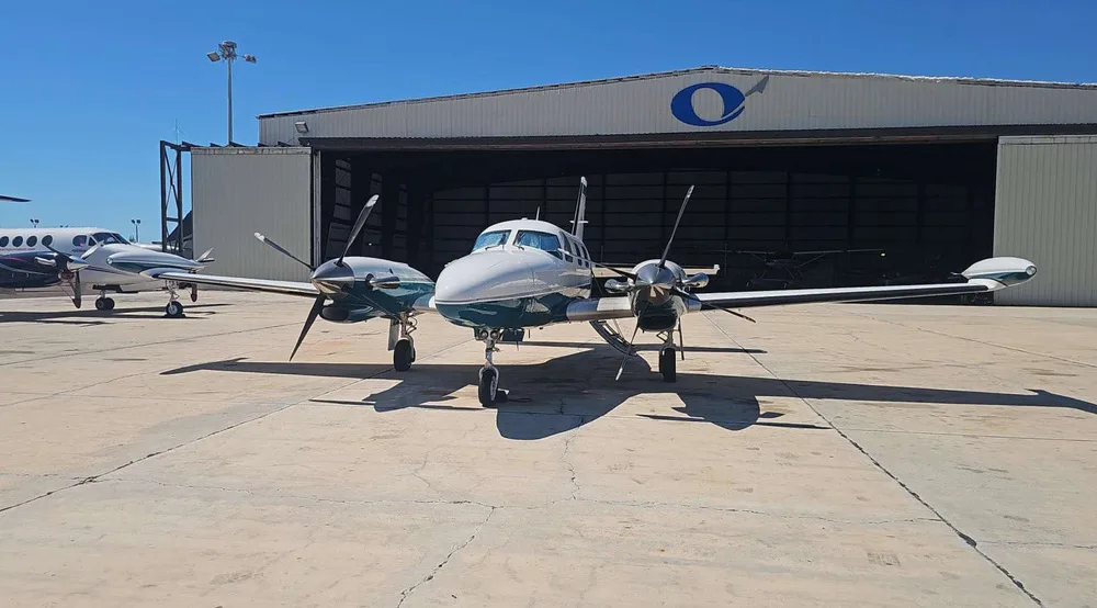 A Piper PA-31 Navajo, registration N444PC, in a white and teal paint scheme, parked on a tarmac in front of a hangar.