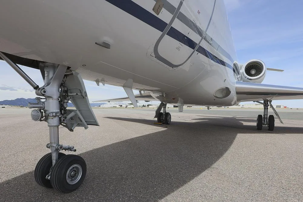 A low-angle view of the main landing gear and underside of a white Dassault Falcon 900 business jet.