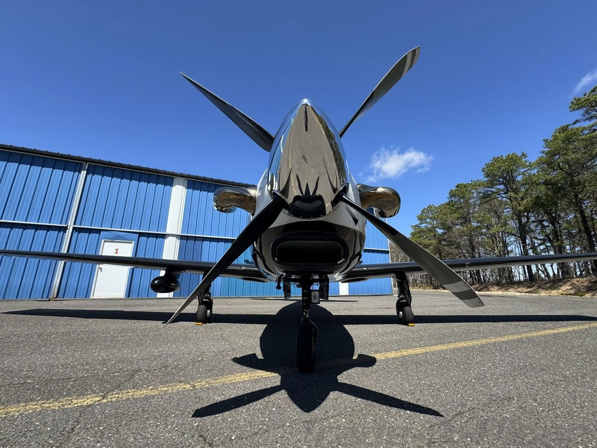 A close-up, low-angle front view of the propeller and shiny nose of a white and black Piper M-class aircraft.