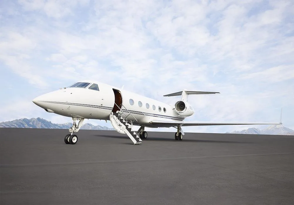 A white Gulfstream G550 business jet with its main door open and airstairs extended on a tarmac.