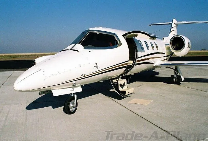 A white Learjet 35A with gold and brown stripes, registration N160GC, parked on a tarmac with its main cabin door open.