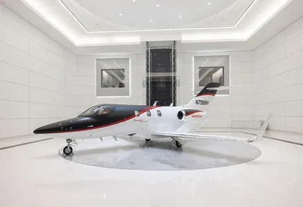 A white HondaJet with black and red accents, registration N798BH, is displayed in a modern, brightly lit white showroom.