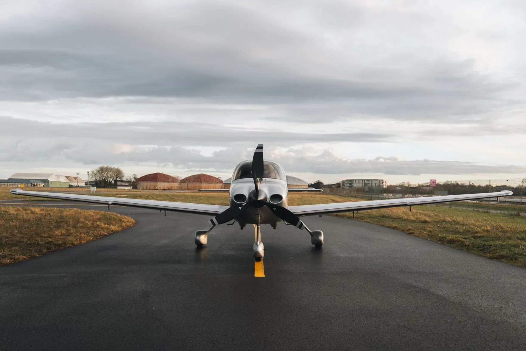 A silver and red Cirrus SR22 aircraft viewed from the front, parked on an airfield under a cloudy sky.