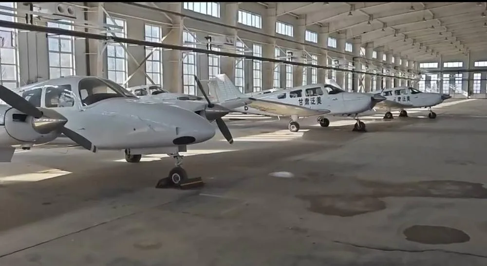 A side view of multiple white propeller aircraft, including twin-engine and single-engine models, lined up in a hangar.