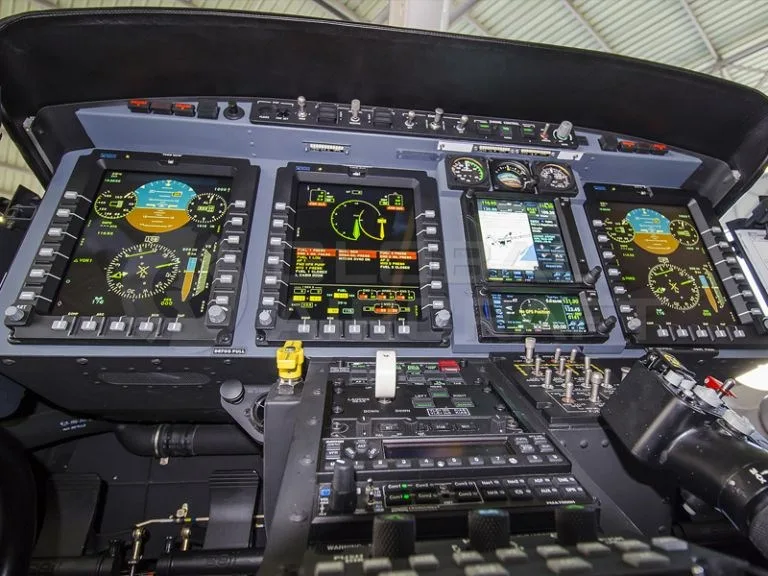 A close-up view of a helicopter's modern instrument panel with multiple digital flight displays.