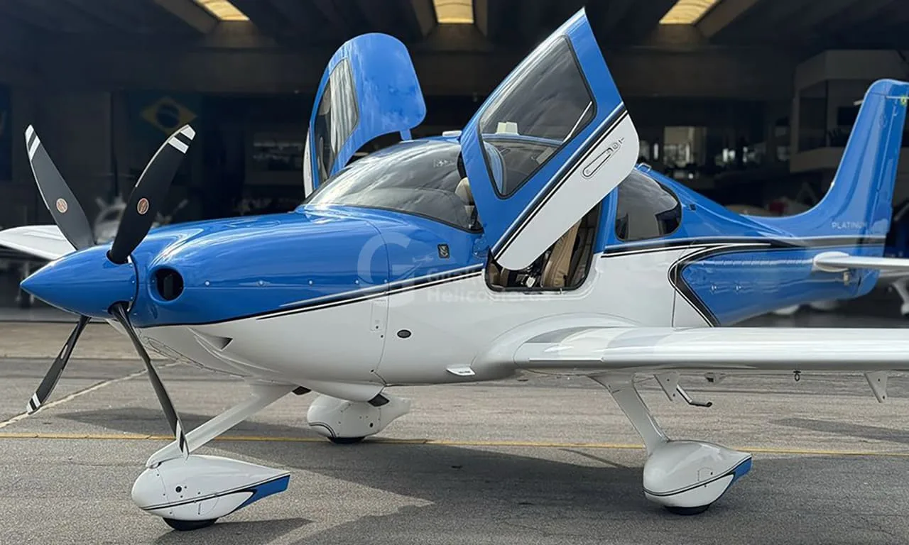 A blue and white Cirrus SR22 aircraft with its gull-wing doors open, parked on an tarmac.