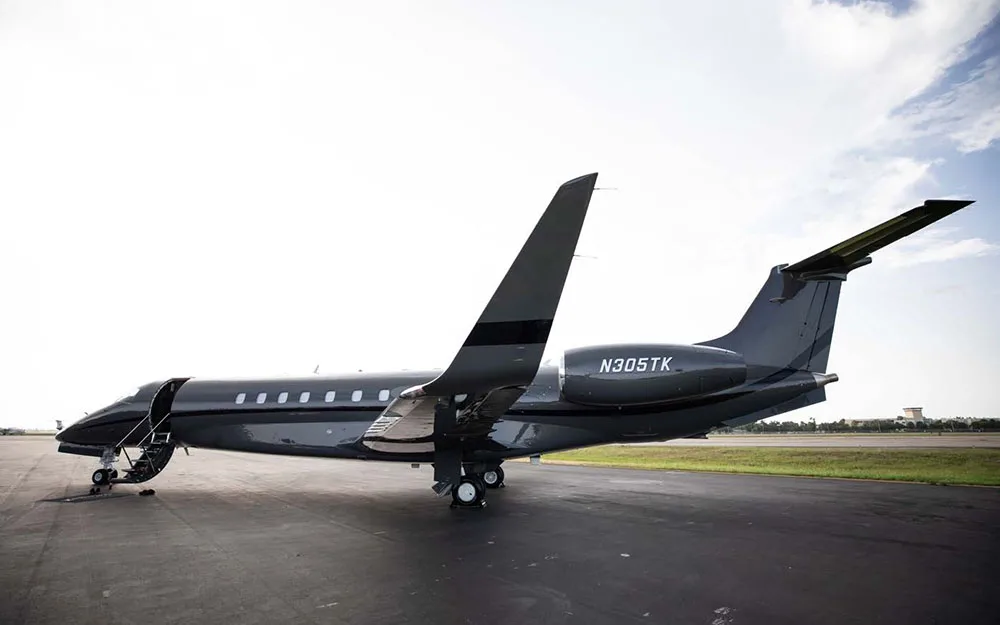A dark grey Embraer Legacy 600 business jet (N305TK) parked on an airfield, viewed from the rear quarter.