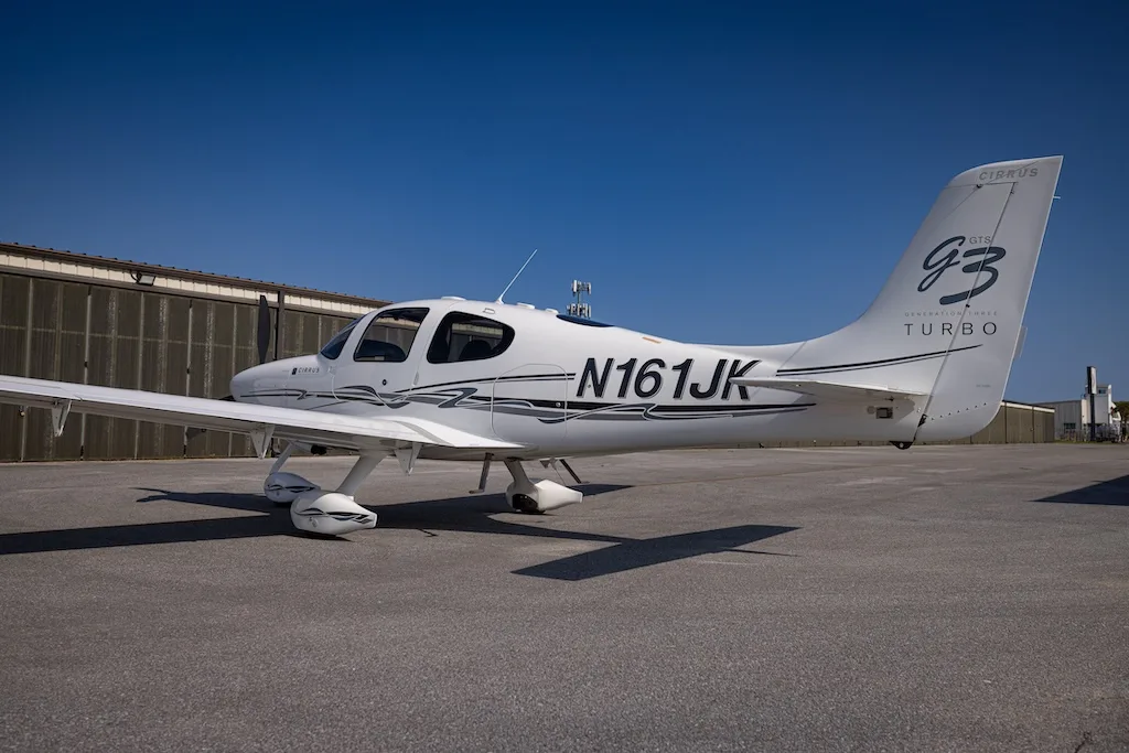 A white Cirrus SR22 G3 Turbo aircraft, registration N161JK, parked on an asphalt tarmac in front of hangars.