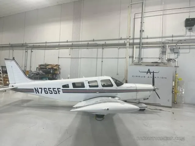 A white single-engine propeller aircraft with black and red stripes, tail number N7655F, parked inside a hangar.