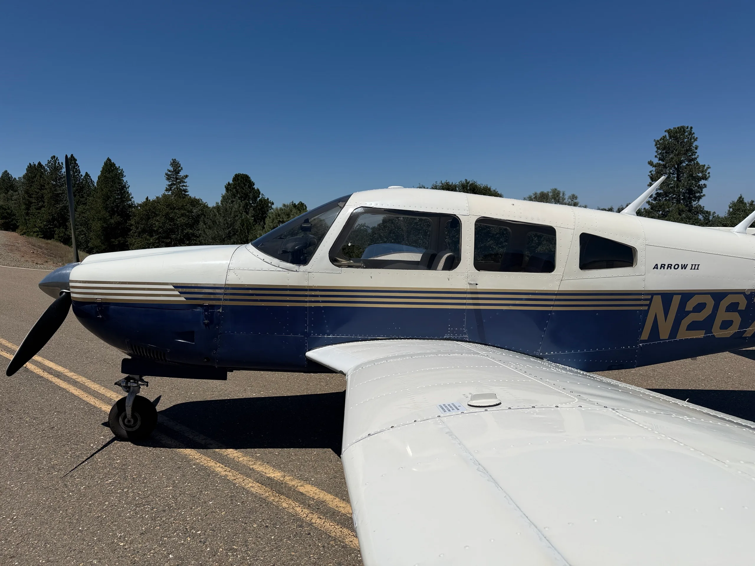 A close-up side view of the cockpit and wing of a white and blue Piper Arrow III aircraft, tail number N2672Q.