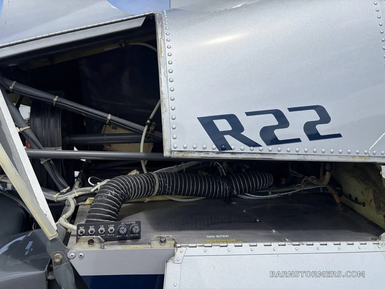 A close-up view of the exposed internal wiring and control panel of a silver Robinson R22 helicopter.