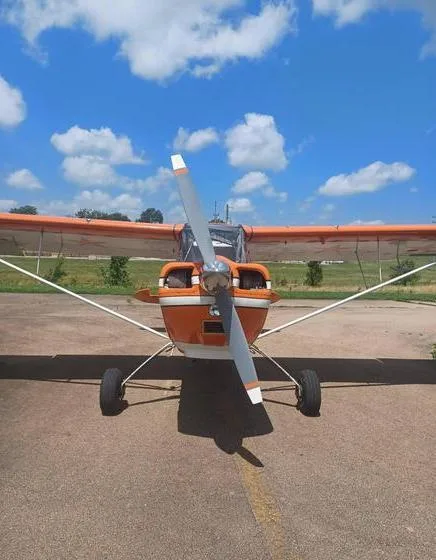 A head-on view of the orange N57411 aircraft, showing its propeller and landing gear against a blue sky.