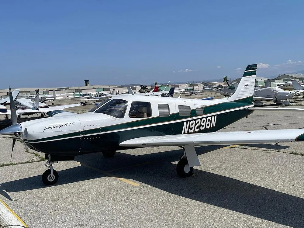 A Piper Saratoga II TC, registration N9296N, in a dark green and white paint scheme, parked on an airfield.