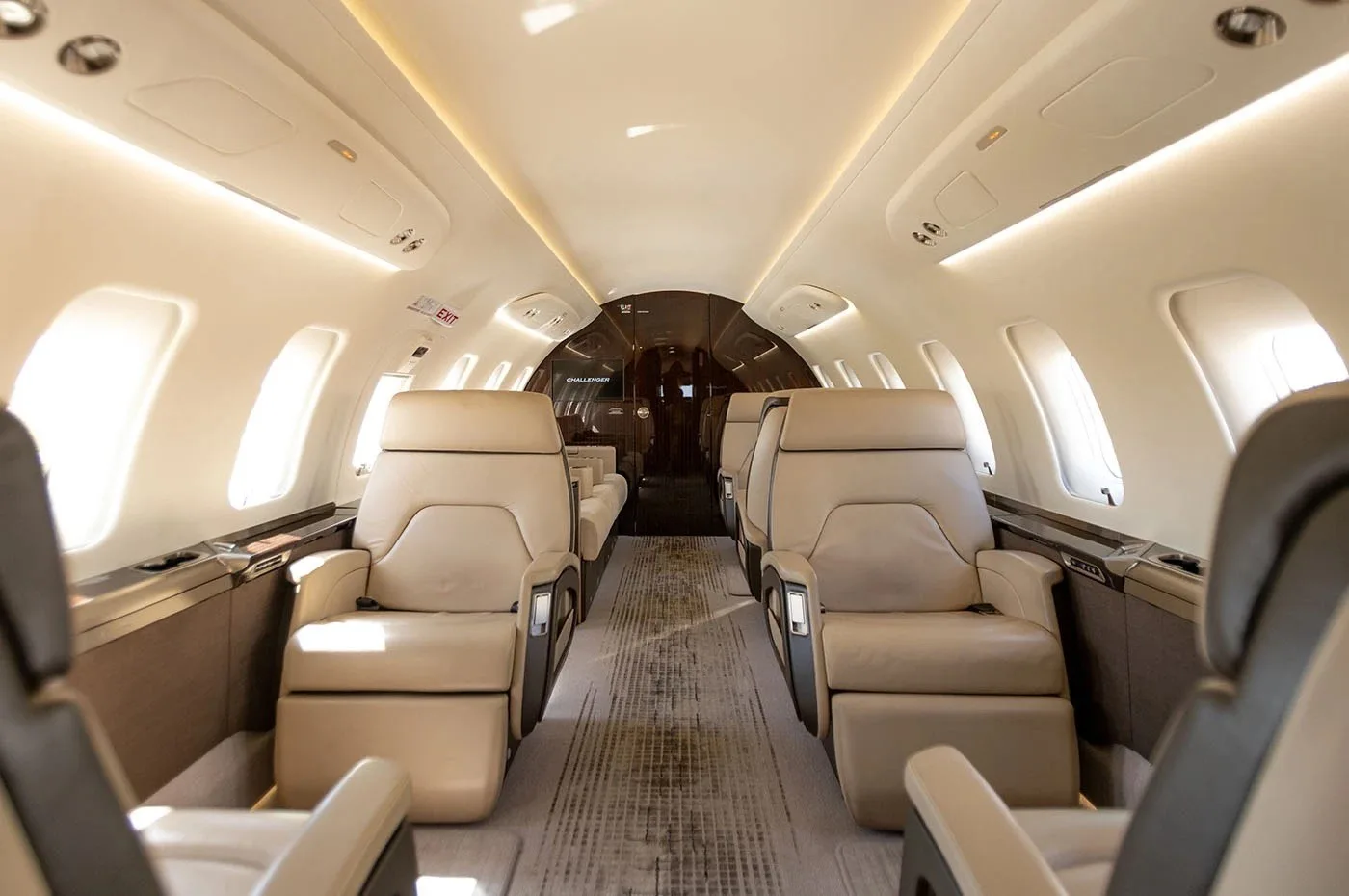 The luxurious cabin interior of a business jet, featuring two rows of beige leather seats facing each other.