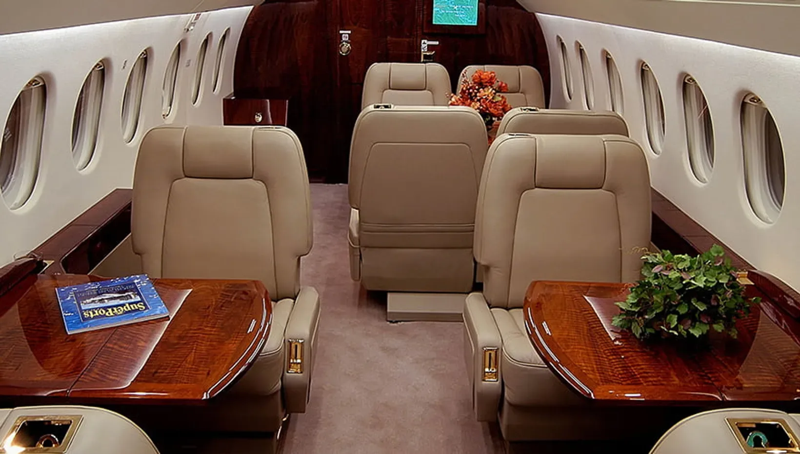 View of a luxurious aircraft cabin interior with beige leather seats and polished wooden tables.