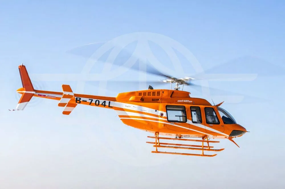 An orange Bell 407EXP helicopter with registration B-704L flies against a clear blue sky, viewed from the side.