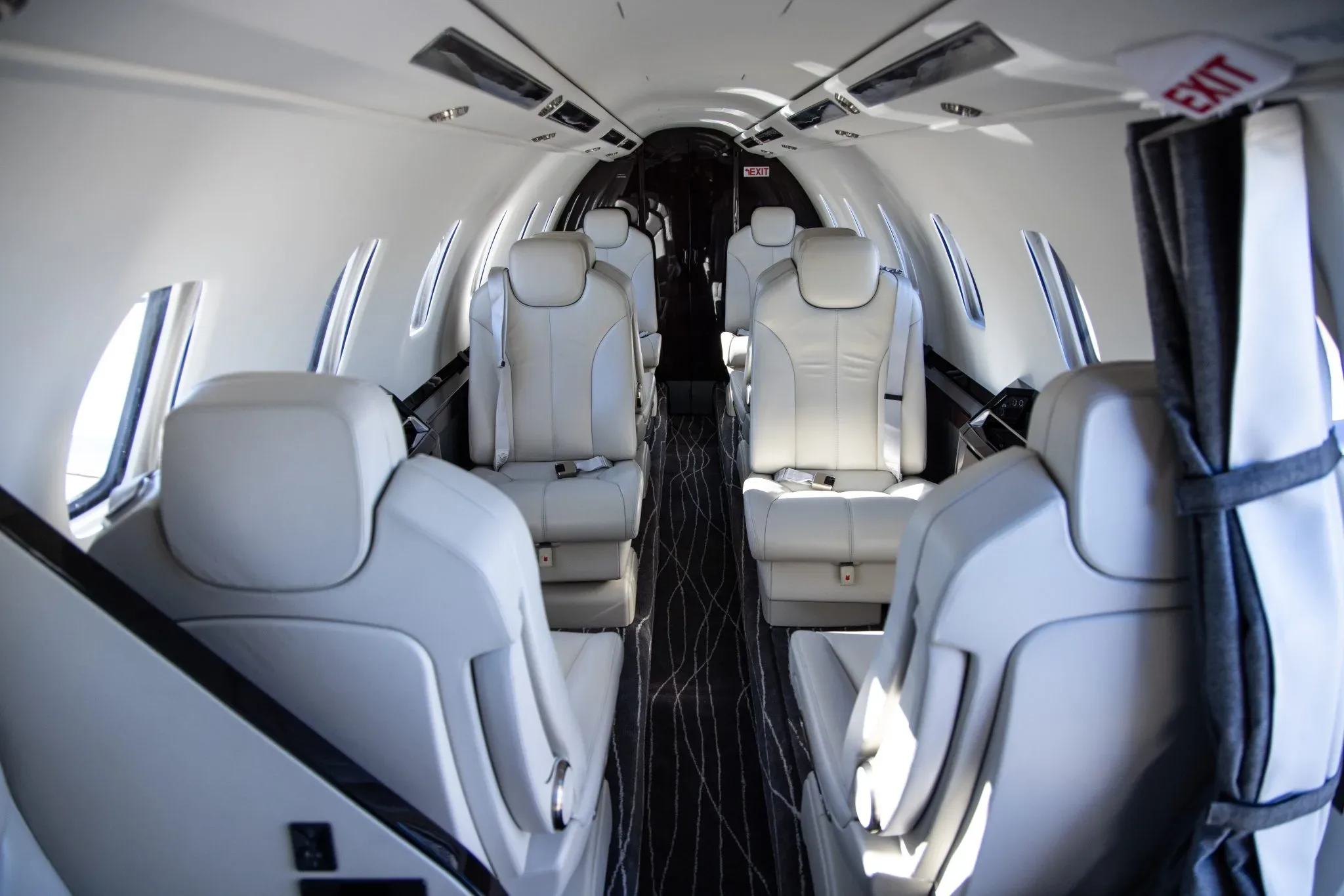 The aircraft cabin features light-colored leather seats arranged in a club configuration with a dark aisle.