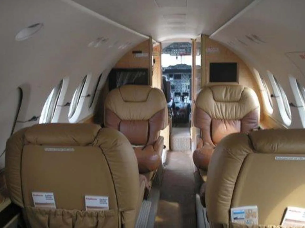 The interior cabin of a private jet with tan and brown leather seats, looking towards the cockpit.