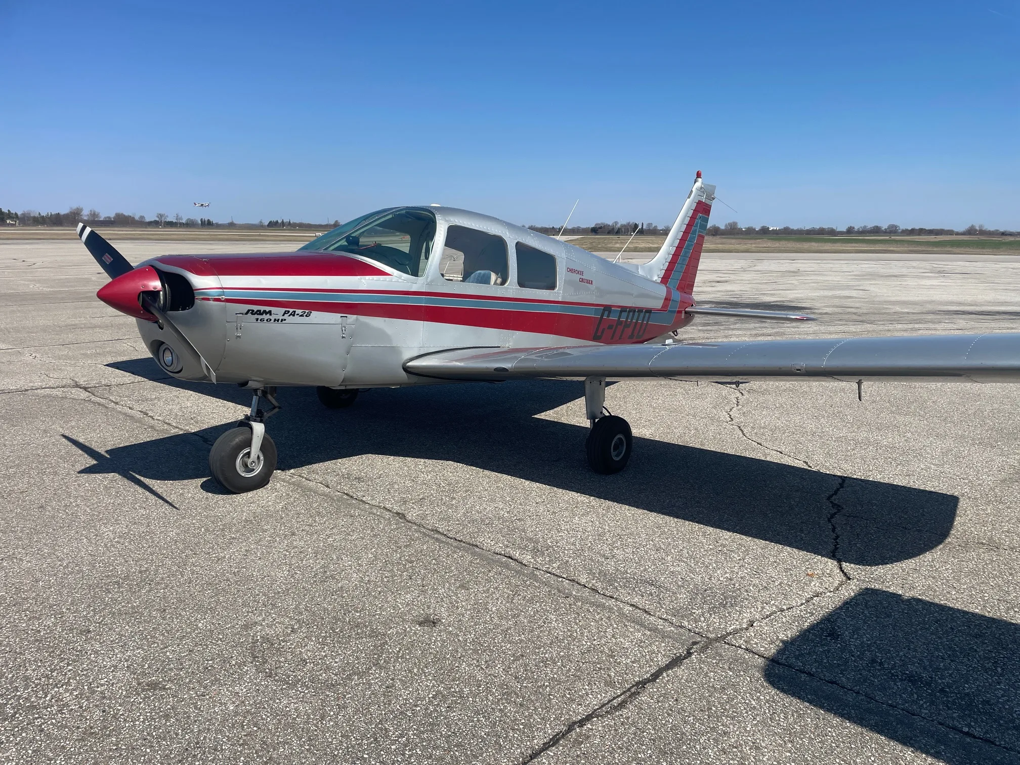 A silver and red Piper PA-28 160HP aircraft parked on an asphalt runway under a clear blue sky.