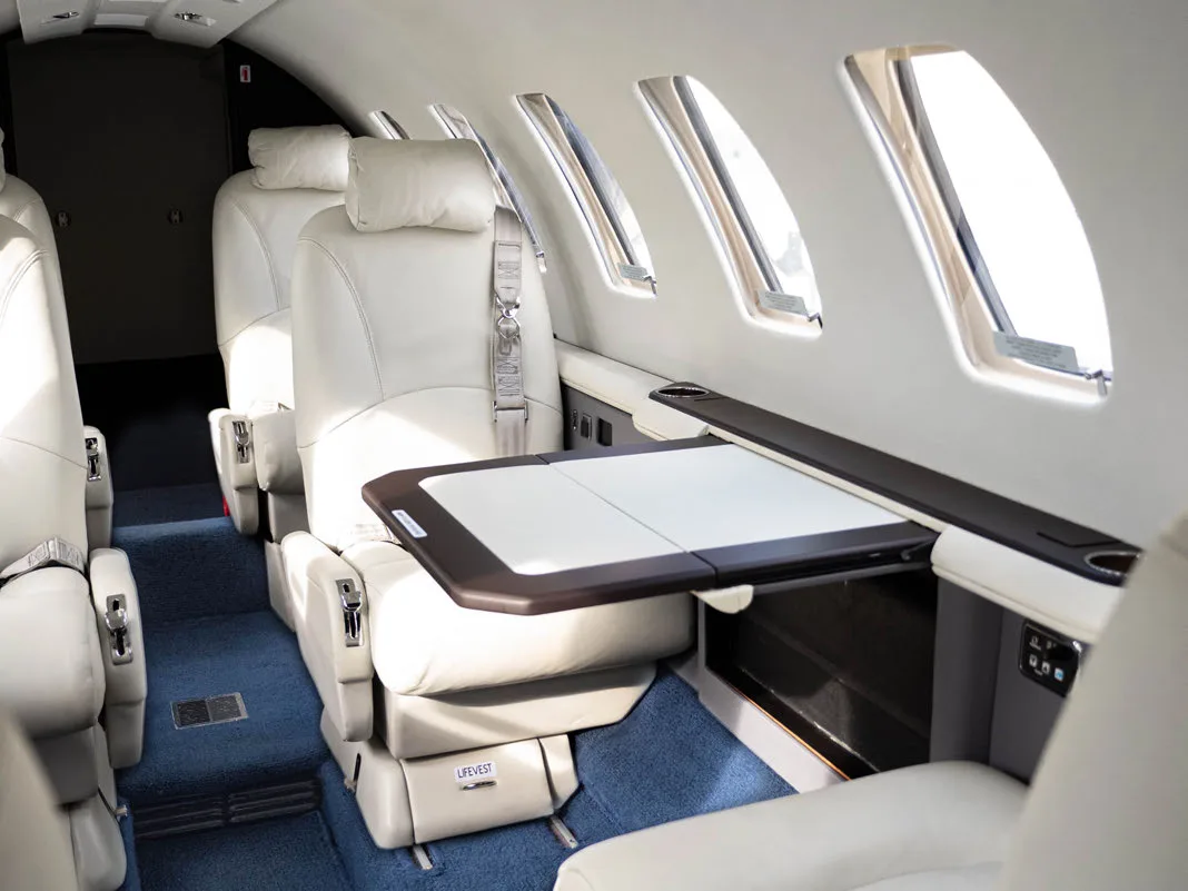 Aircraft interior with white leather seats and a fold-out table.