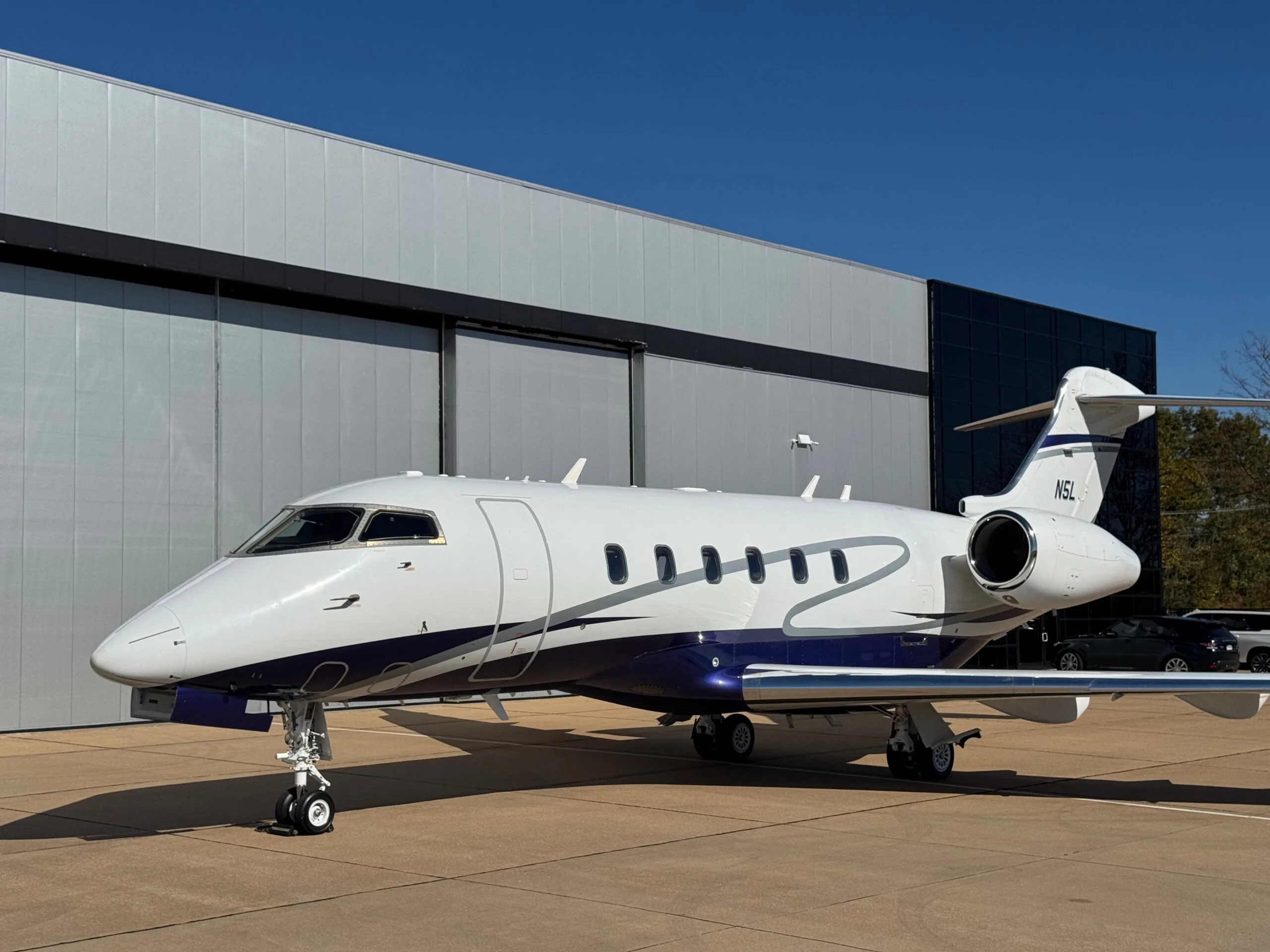 Three-quarter front view of the N5L business jet, a white aircraft with blue and silver stripes, parked on an airfield.