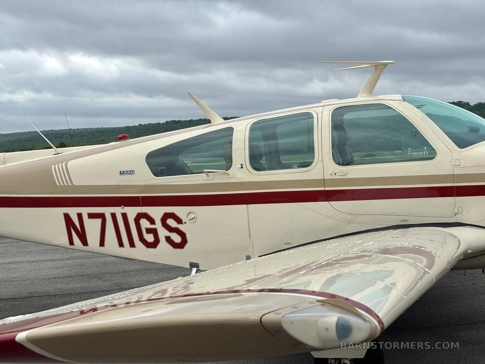A close-up side view of the cream and red Beechcraft Debonair N711GS on the tarmac.