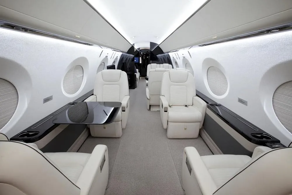 The interior cabin of a business jet showing cream leather seats and a deployed dark table.