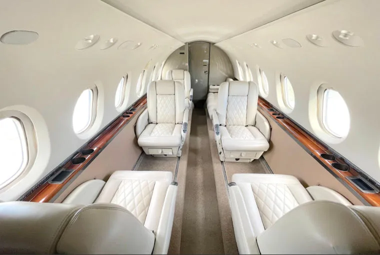 The aircraft's interior cabin features light-colored quilted leather seats and wood trim.