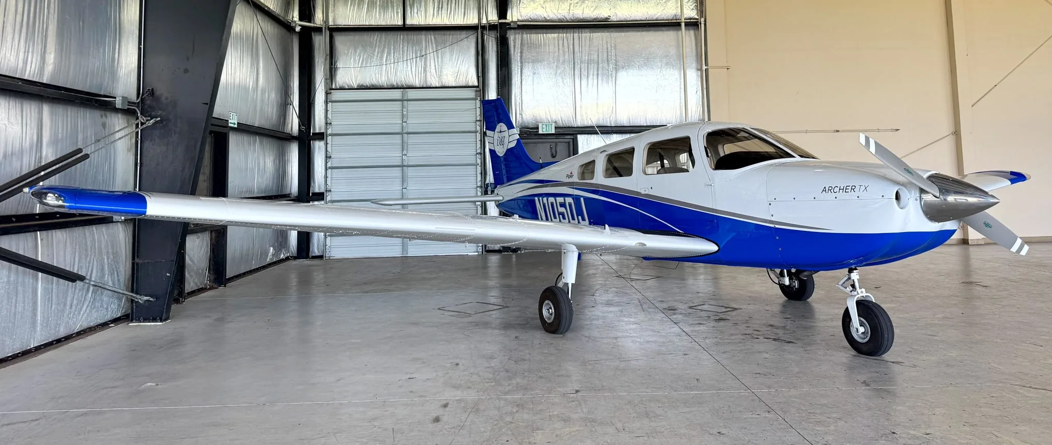The white and blue Piper Archer TX aircraft, N105DJ, is seen from the front-right in a hangar.